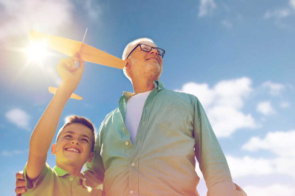 A grandfather and grandson playing with a toy plane outdoors.